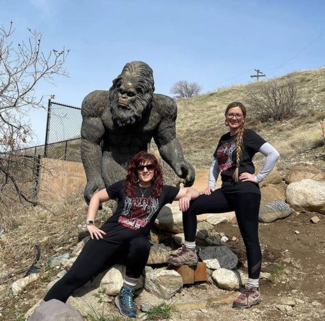 Two women in monsters among us tee shirts standing next to a bigfoot statue 